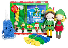 Crochet kit with elf dolls, blue narwhal, and yarn in front of 'Elf' movie poster packaging.