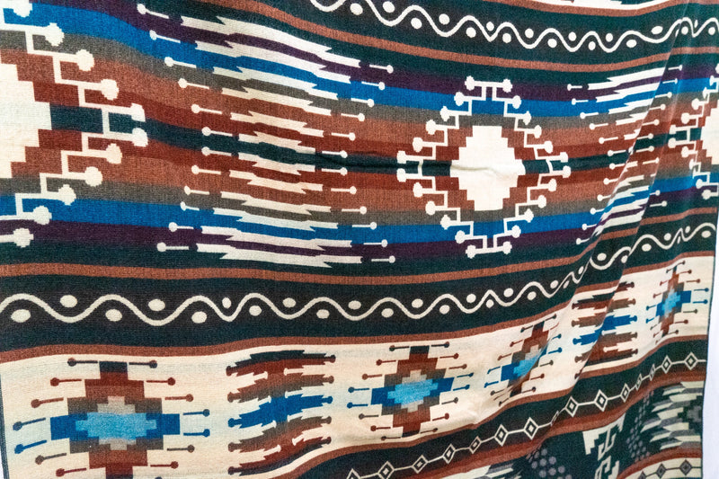 Close-up of the Evergreen blanket laid flat, emphasizing the cream and multi-color diagonal geometric motifs.