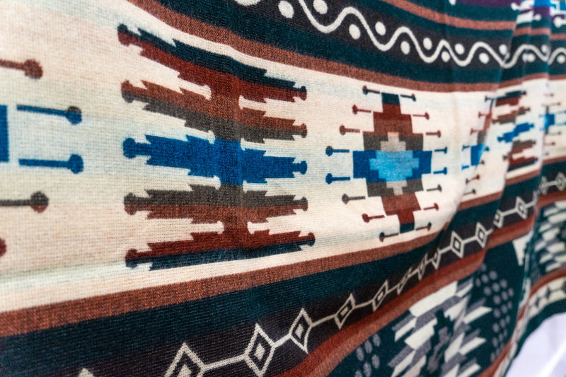 Wide close-up of the Evergreen blanket's central section, showing the horizontal stripe bands, wave motifs, and cream geometric center.