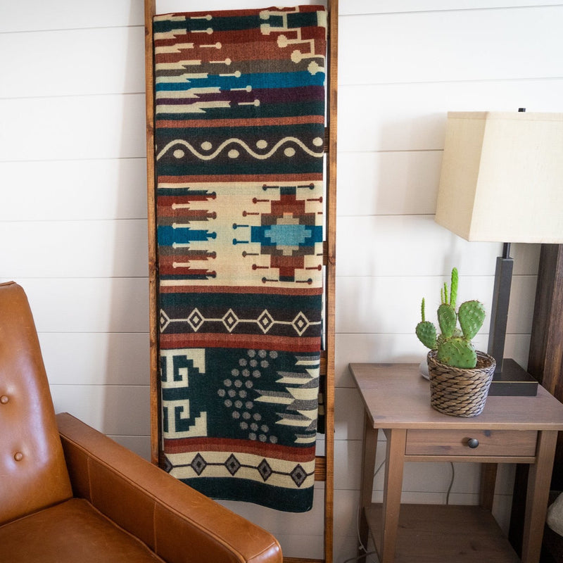 Evergreen Alpaca Blanket draped fully on a tall wooden ladder, showcasing the intricate horizontal pattern bands in teal, burgundy, and cream in a rustic room.