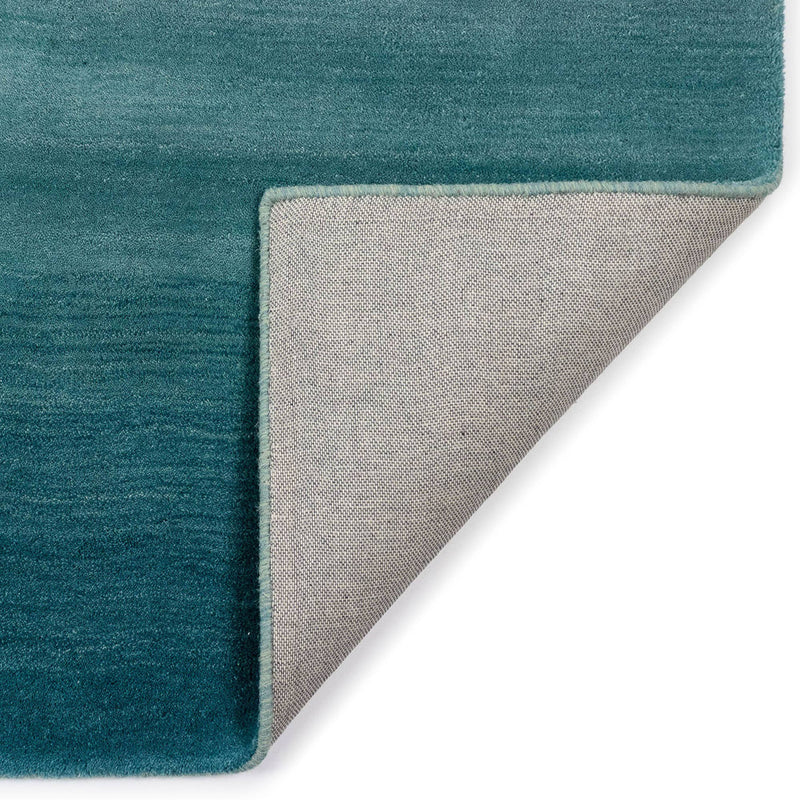 A folded corner of the luxurious blue ombre indoor rug measuring 5'x7'6", made of 100% hand-loomed wool with a sophisticated contemporary design.