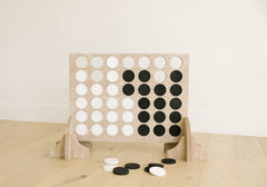 Wooden connect four game with black and white discs on a wooden surface.