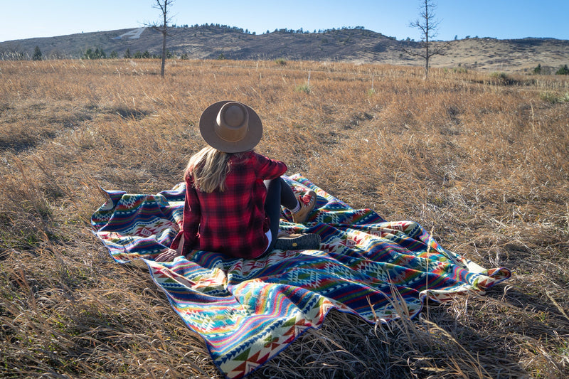 Close-up of the Galapagos Blanket draped over her knees, showing the intricate details of the colorful geometric stripes.