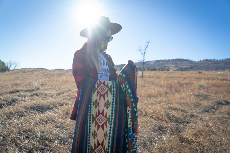 Woman holding the Galapagos Blanket folded horizontally in half, standing in the middle of the golden field.