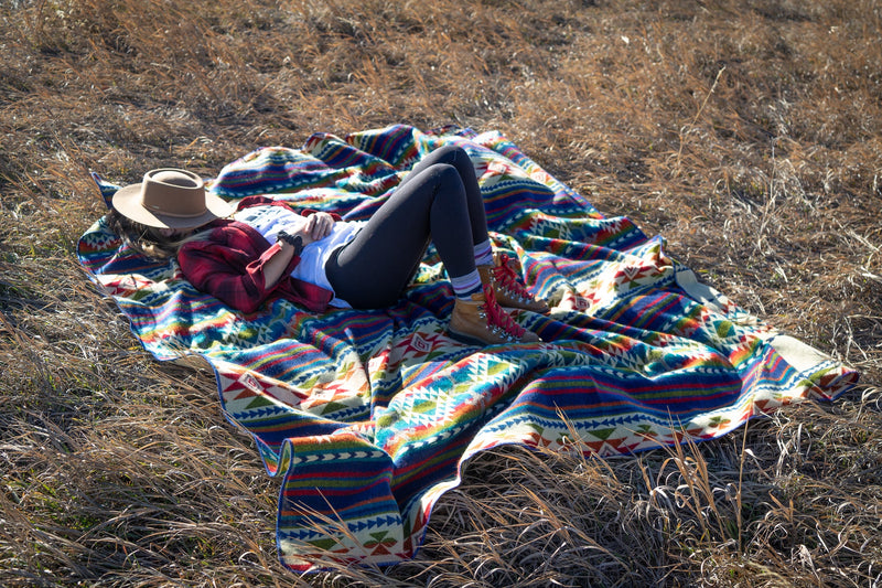 Close-up of the Galapagos Blanket folded and resting on the grassy ground, highlighting the textures and contrast.