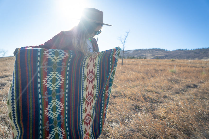 Woman sitting on the ground with the Galapagos Blanket spread out around her, showing its use as a picnic or camping blanket.