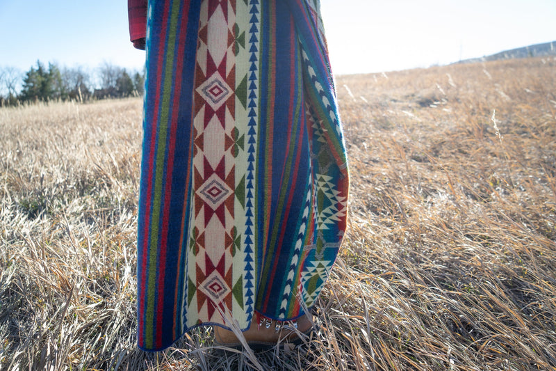 Woman holding the Galapagos Blanket up near her face, with the sun creating a soft halo and highlighting the vibrant colors.