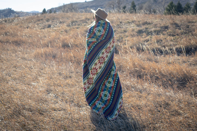 Woman seen from the back, fully wrapped in the Galapagos Alpaca Blanket, standing in the center of the field.