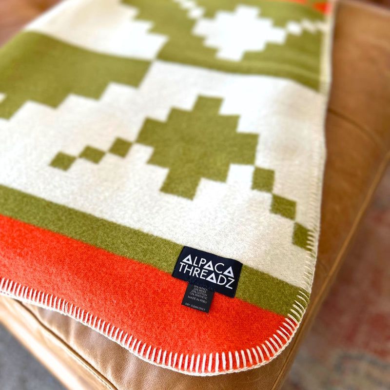 Corner detail of the green and red geometric alpaca blanket showing the clean white background and the small brand logo tag.
