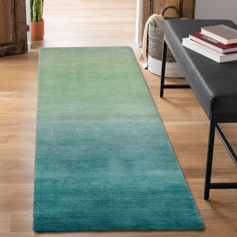 A luxurious blue ombre indoor rug measuring 5'x7'6" located in a hallway to a home, made of 100% hand-loomed wool with a sophisticated contemporary design.