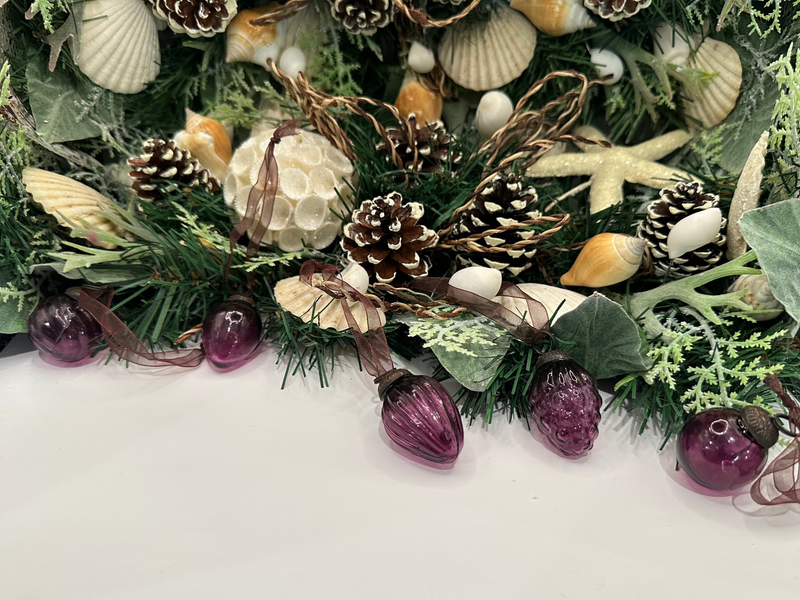 A set of five small hand-blown crackle baubles in a mulberry color, hanging among greenery, seashells, and pinecones, with ornate caps and sheer brown ribbon ties.