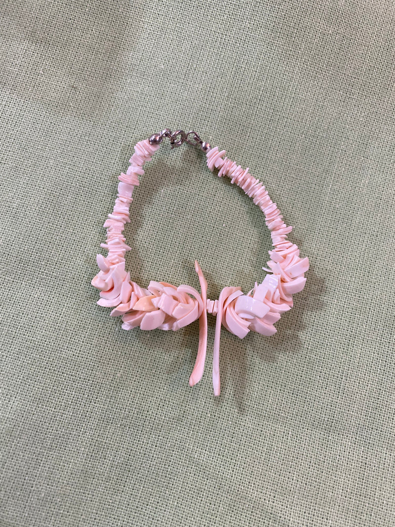 Vintage pink carved shell bracelet with layered floral-inspired details, displayed on a soft green fabric background.