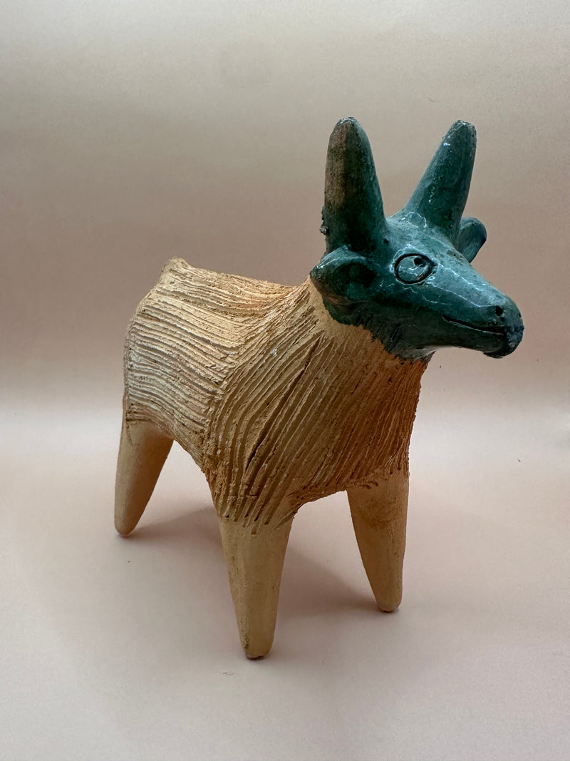 Side angle of a vintage terra cotta sheep chia pet, highlighting the textured tan body and the green-glazed head with detailed horns.