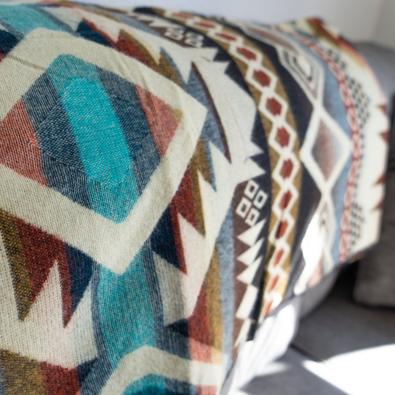 Corner view of the Inca Alpaca Wool Blanket draped over a couch, with light catching the reversible design and earthy tones.