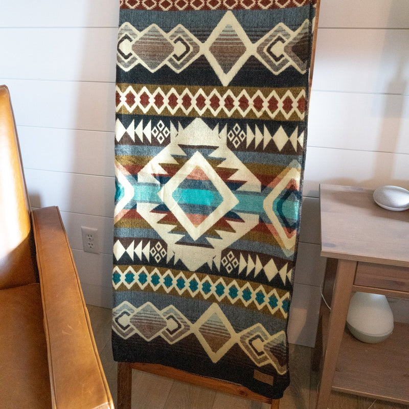The Inca Alpaca Wool Blanket hung vertically, showcasing its full tribal pattern and reversible colors, against a light background.