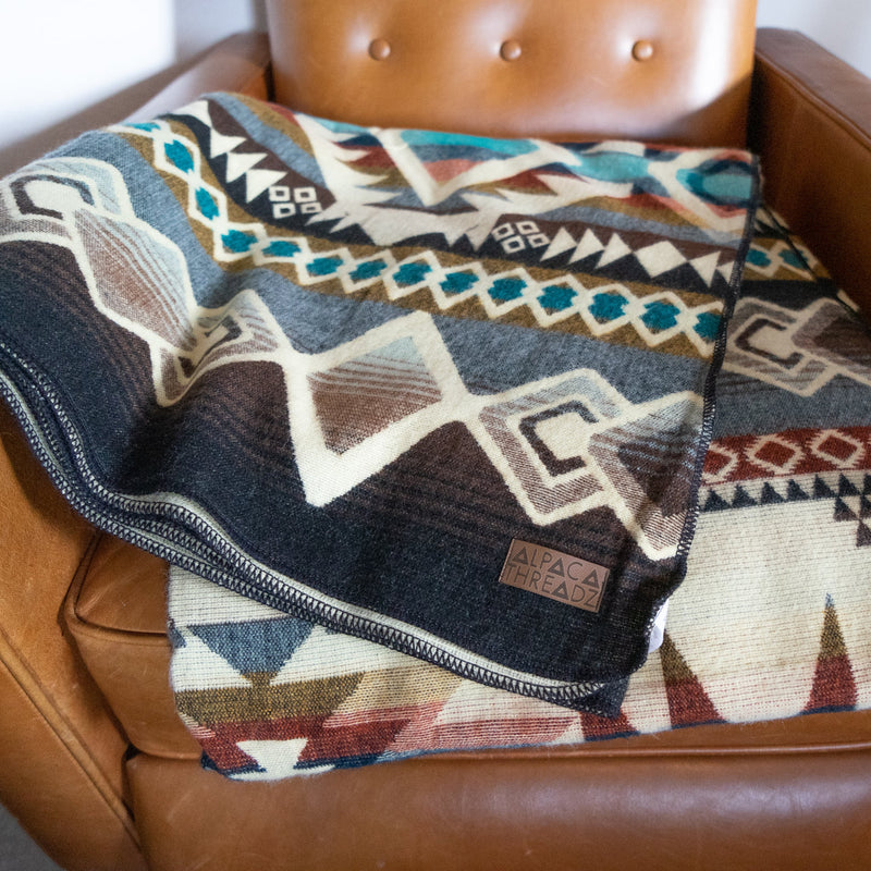 Close-up of the Inca Alpaca Wool Blanket draped over a brown leather armchair, emphasizing its warmth and rich design.
