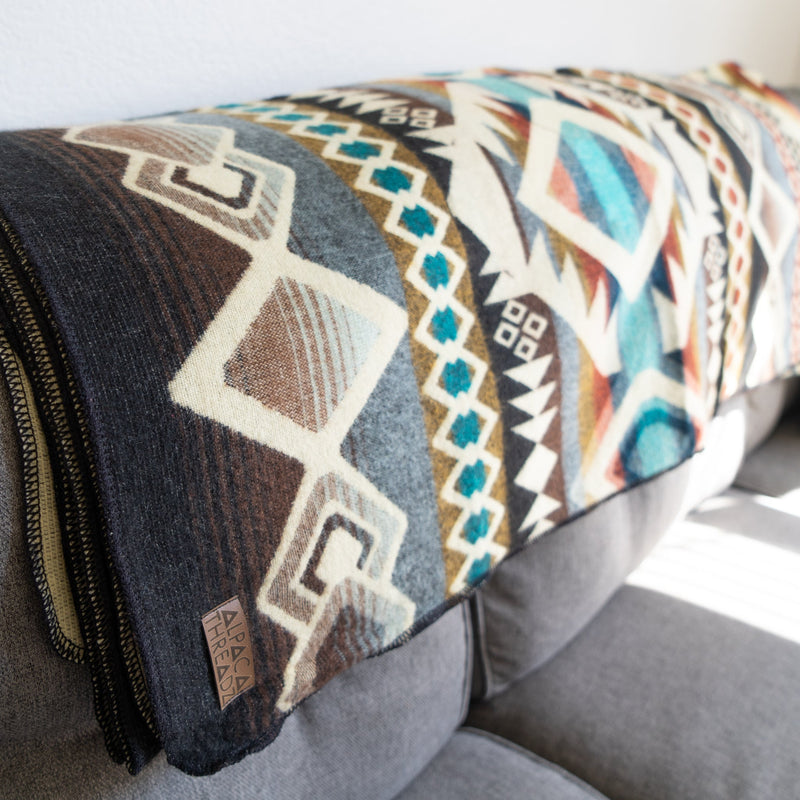 The Inca reversible Alpaca Wool Blanket draped over a grey sofa, showcasing its intricate tribal design and texture.