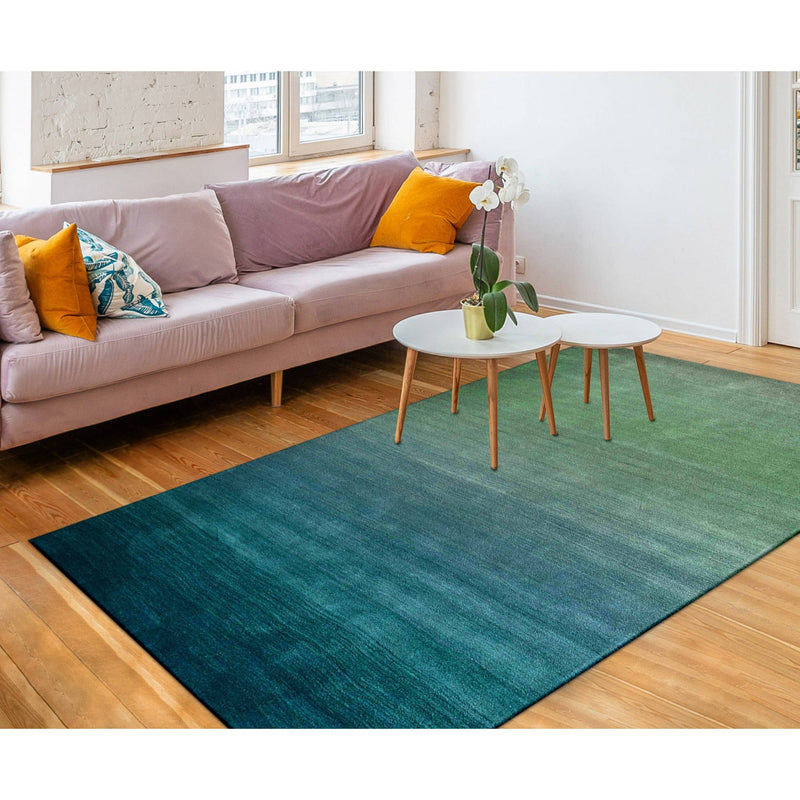 A luxurious blue ombre indoor rug measuring 5'x7'6", shown in a living room with a couch and 2 coffee tables. Made of 100% hand-loomed wool with a sophisticated contemporary design.