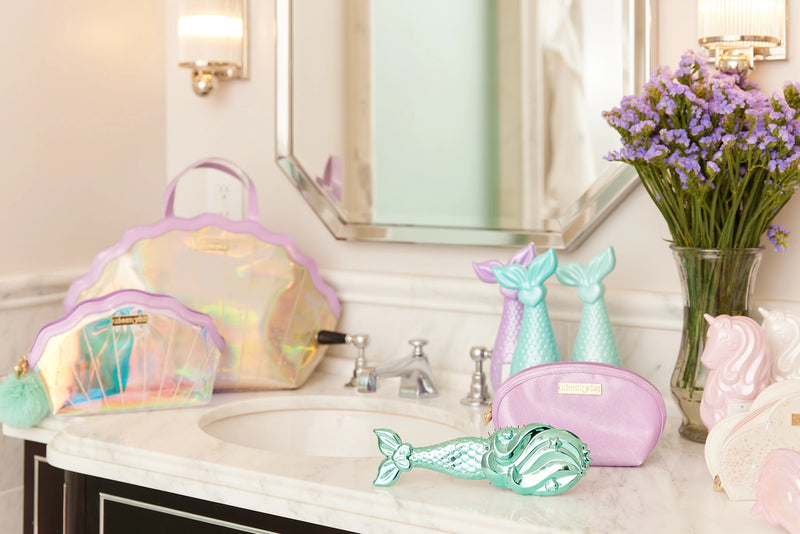 Aqua mermaid hairbrush displayed on vanity with pastel beauty accessories.