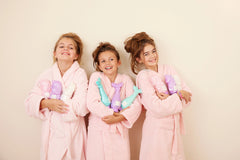 Group of kids in robes smiling and holding Mermaid Shampoo bottles.