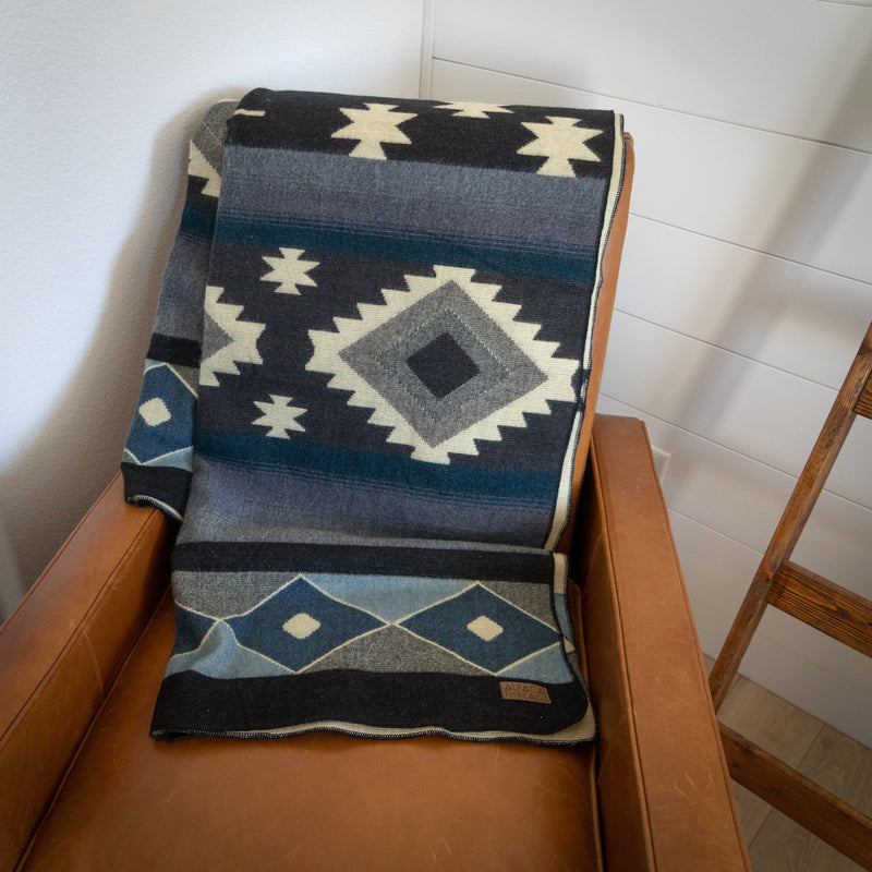 Midnight Blue & Grey Alpaca Blanket folded and draped over the back of a patterned armchair, showing the elegant color combination.