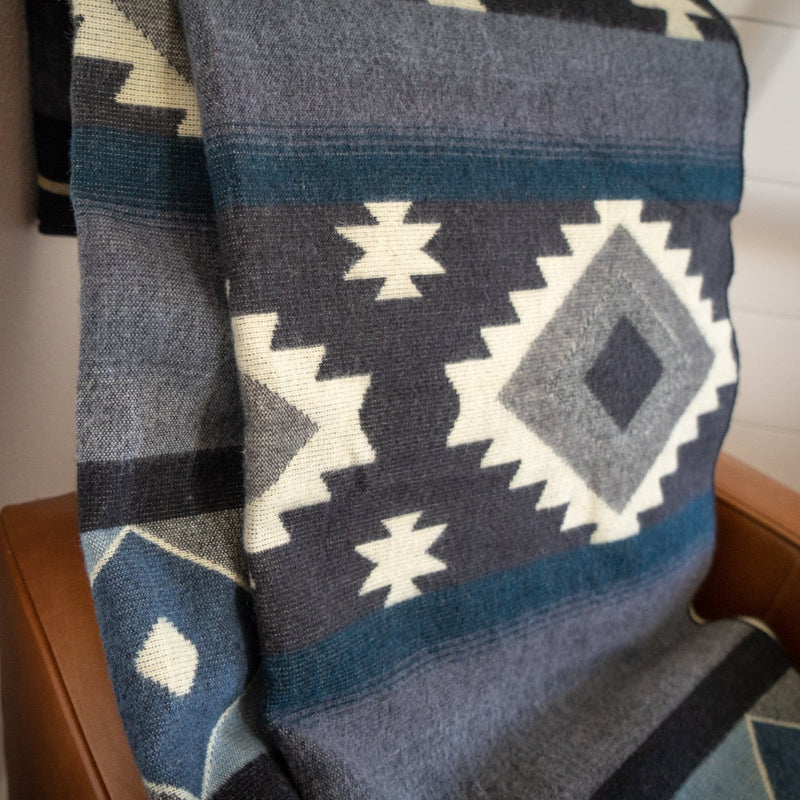 Woman holding the Midnight Blue & Grey Blanket spread out, showcasing the full complex geometric pattern.