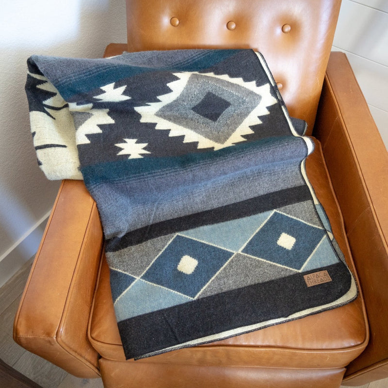 Midnight Blue & Grey Alpaca Throw folded neatly on a brown leather accent chair.
