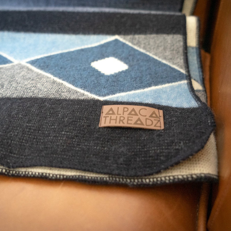 Close-up of the corner of the Midnight Blue & Grey Throw resting on a leather surface, clearly showing the stitched leather brand tag.