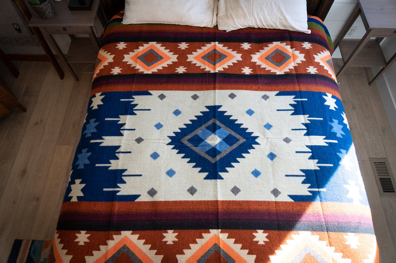 Full view of the reversible side of the Andean Alpaca Blanket, featuring a different color distribution with a dominant cream and blue pattern on the bed.