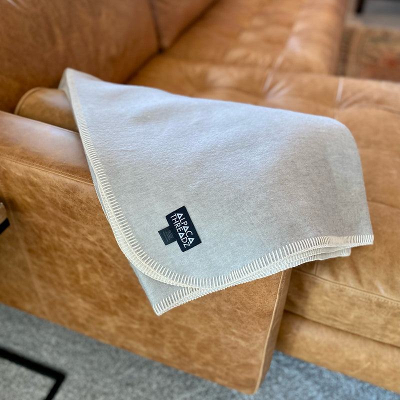 Blue fleece throw blanket folded on a hardwood floor, revealing the soft off-white sherpa reverse side and the cream blanket stitch edging