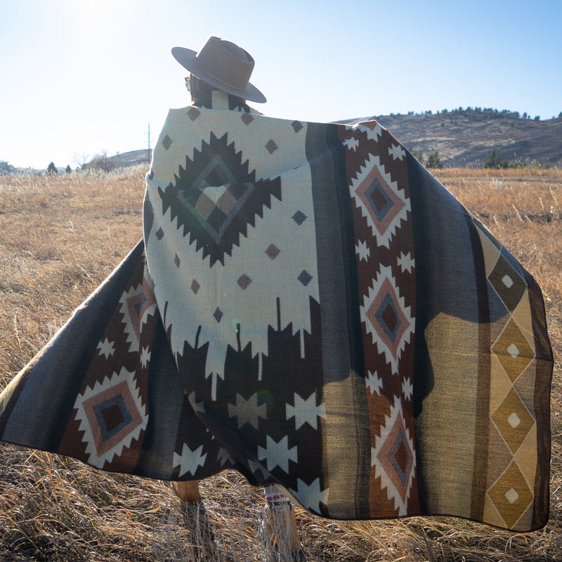 Woman seen from the back holding the Mojave blanket draped, showcasing the cream and brown geometric design.