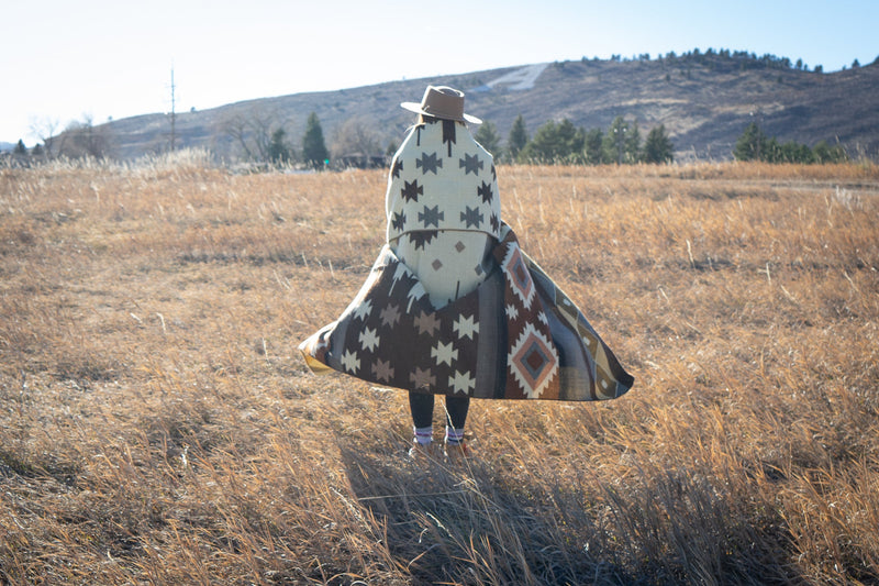 Mojave alpaca blanket folded and held by a woman standing in profile in the grassy, outdoor landscape.