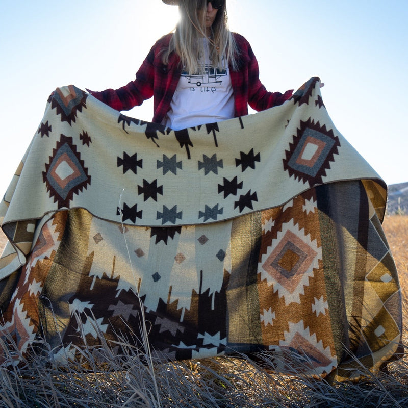 Woman holding the Mojave blanket out horizontally, showing the full width and stripe pattern detail in the field.