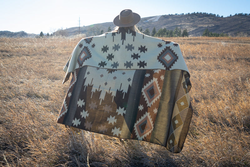Woman holding the Mojave blanket draped over her head, with the sun shining directly from behind, illuminating the geometric pattern.