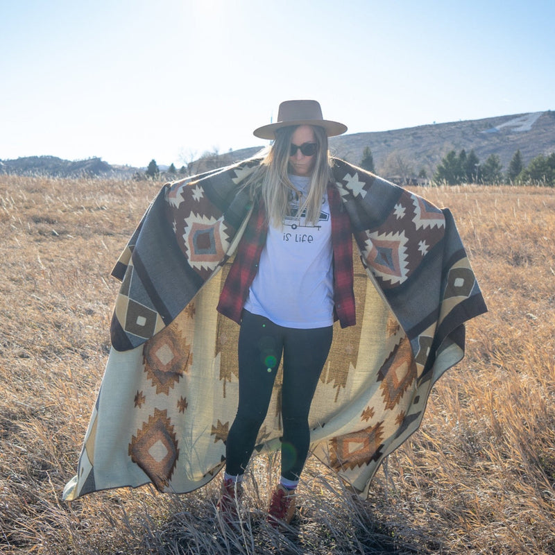 Woman walking towards the camera, holding the Mojave blanket fully draped down to the ground in an outdoor setting.