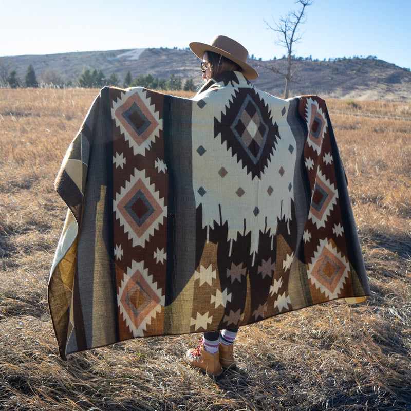 Woman fully wrapped in the Mojave alpaca blanket in a grassy outdoor field, highlighting the blanket's warmth and large size.