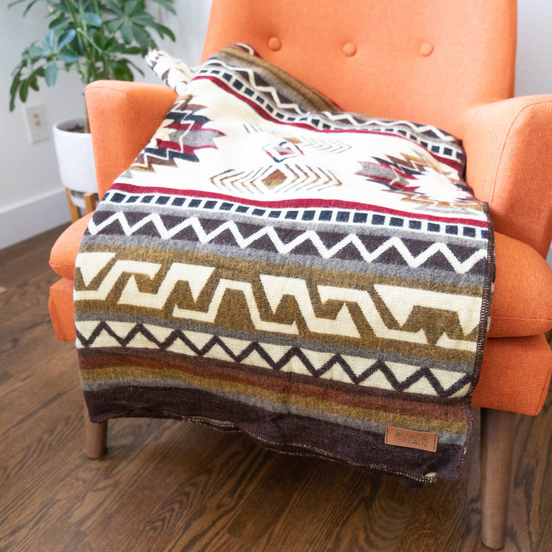 The reversible Mountain Alpaca Blanket draped over a vibrant orange accent chair, emphasizing its use as a stylish home decor throw.