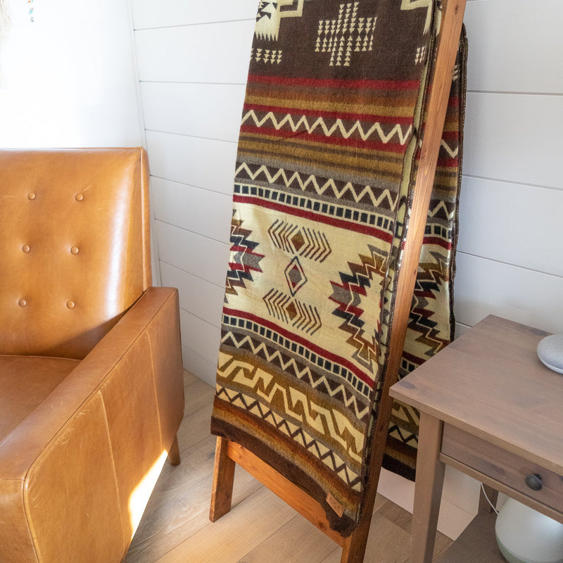 Full length view of the Queen-size Mountain Alpaca Blanket draped over a brown chair in a brightly lit, rustic corner.
