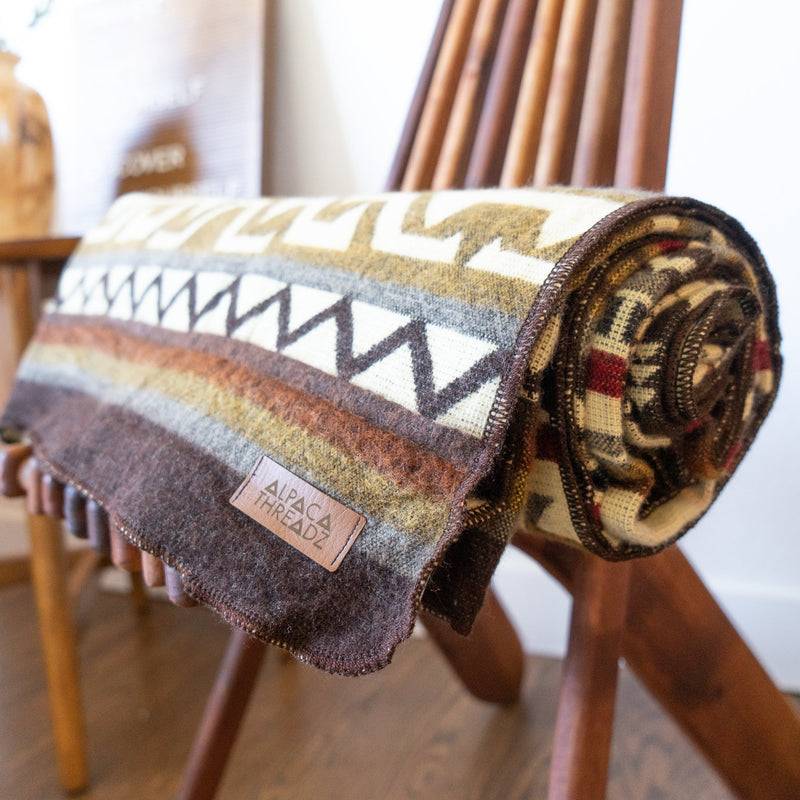 The Mountain Alpaca Wool Blanket rolled up and resting on a wooden surface, demonstrating its portability and texture.