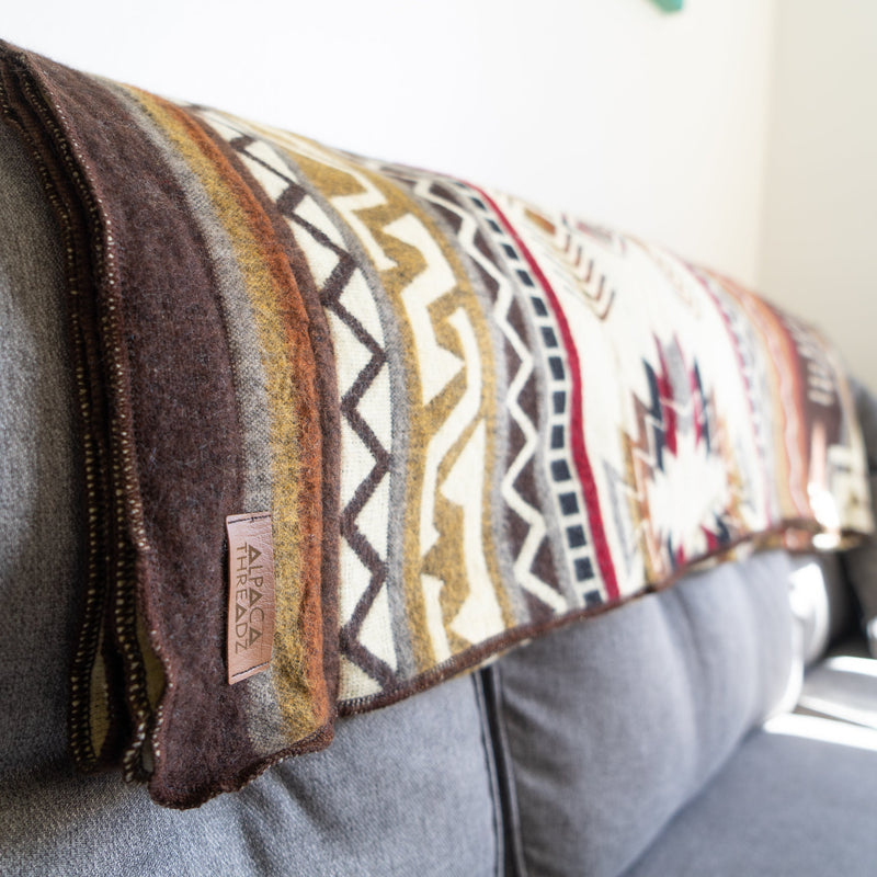 Side view of the Mountain Alpaca Wool Blanket draped over a gray sofa, highlighting the earthy colors and cozy texture.