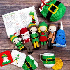 Collection of crocheted characters and items on a wooden surface with a crochet pattern book.