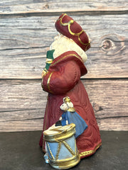 Ceramic Santa figurine in a burgundy robe, holding a nutcracker and ballerina, surrounded by ballet slippers, toy soldiers, and a Christmas tree, with intricate gold accents.