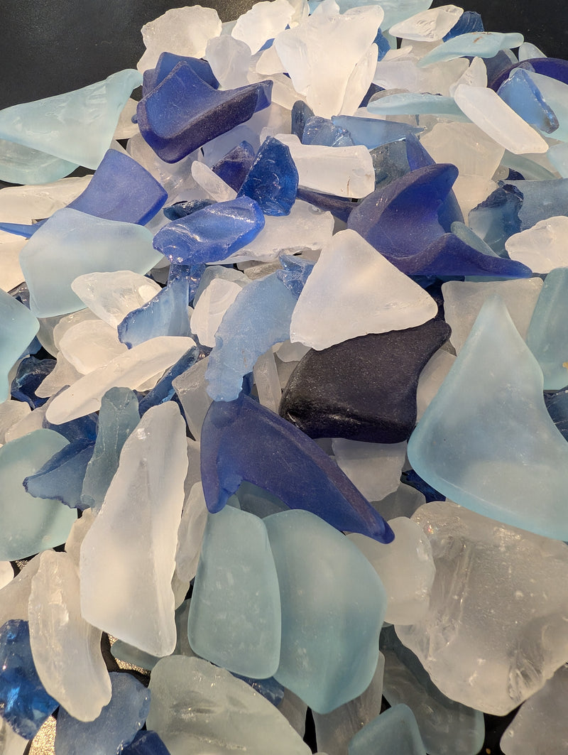 Close-up of dark blue, light blue, and clear hand-tumbled sea glass in various sizes and shapes.