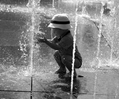 Child playing with water fountain in black and white photo