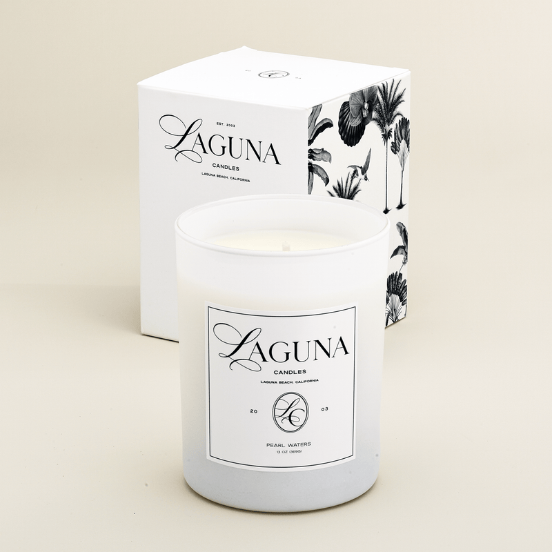 Laguna Candles Pearl Waters 13oz luxury candle in white frosted glass, displayed next to its gift box with black and white tropical botanical illustrations.