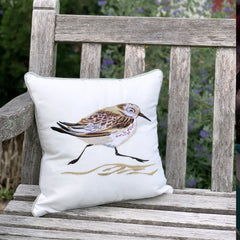 Piper Sprinting Right Pillow featuring a sandpiper embroidery on a crisp white panel, displayed on a wooden bench outdoors.