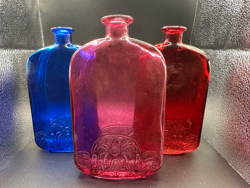 A photo of our Plum, Red, and Blue bottles under light. Plum in the front, blue and red in the back.