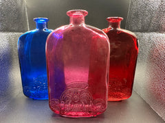 A photo of our Plum, Red, and Blue bottles under light. Plum in the front, blue and red in the back.