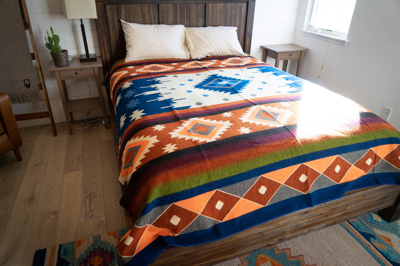 Full view of the reversible Moab Alpaca Wool Blanket covering a Queen bed with a wooden headboard, highlighting its size and colors in a bedroom setting.