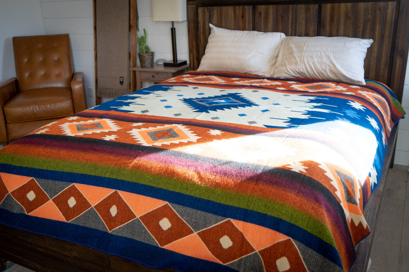 Wide shot of the Andean Alpaca Wool Blanket (Moab) on a bed, emphasizing the terracotta, blue, and burgundy tones against a natural backdrop.
